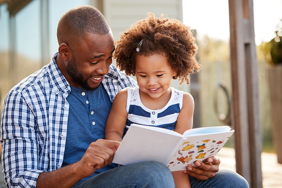 A young father enjoys reading a book aloud to his daughter