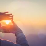 A woman makes a frame with her hands around the sun.