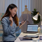 a woman business owner sitting at her desk in her office while smiling at her phone
