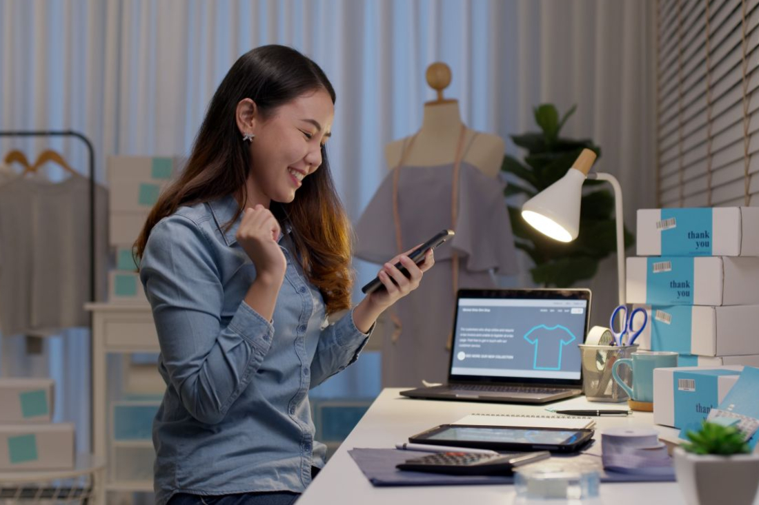 a woman business owner sitting at her desk in her office while smiling at her phone