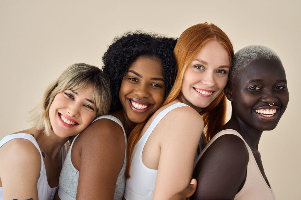 Happy multicultural girls hugging on beige background