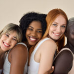 Happy multicultural girls hugging on beige background