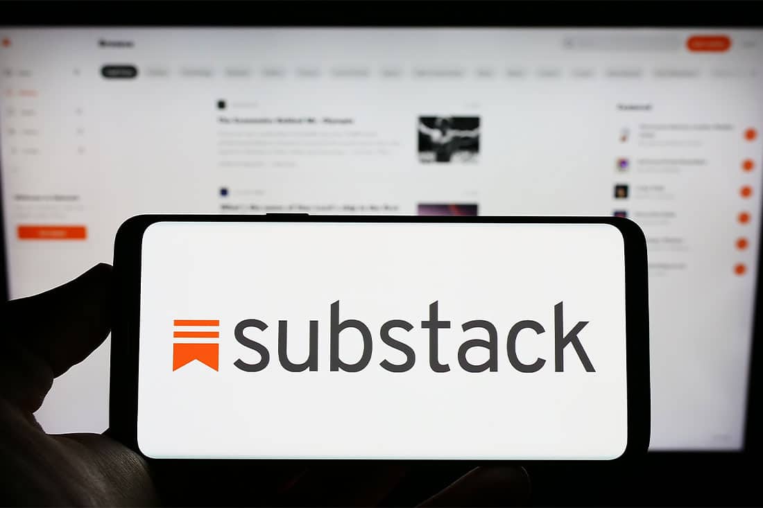 Person holding cellphone with logo of subscription company Substack on screen in front of business webpage
