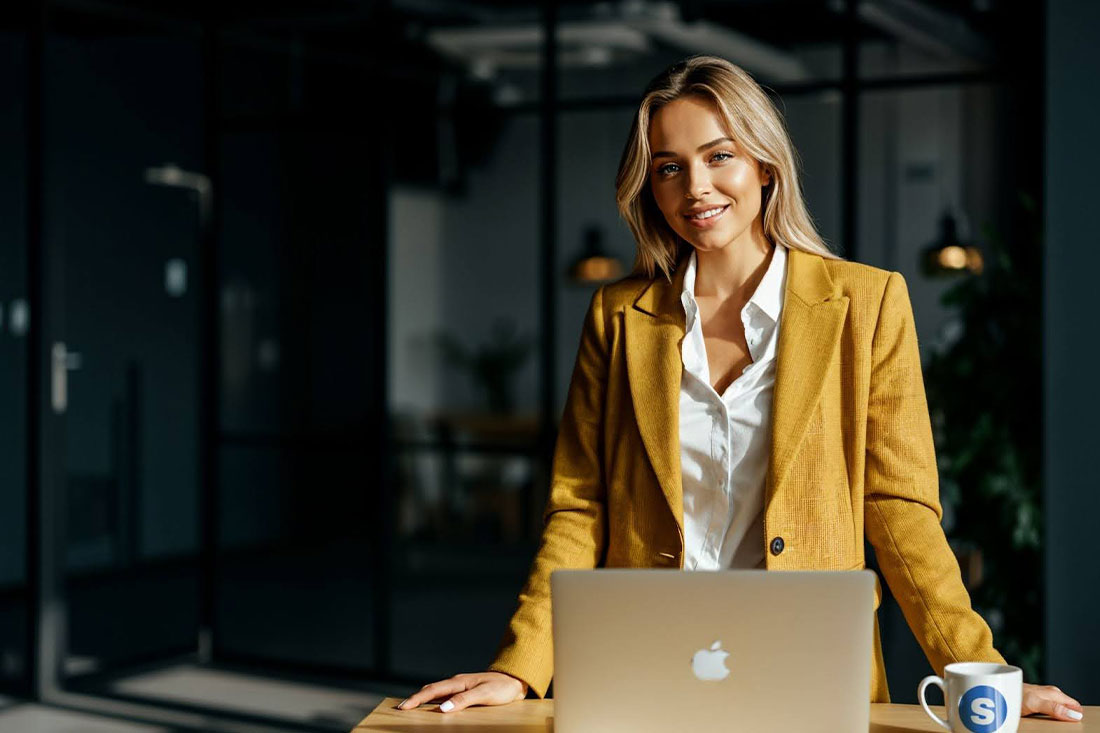 woman in yellow blazer standing in front of open apple laptop
