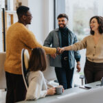 A woman greets a man in an office and shakes his hand