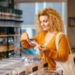 Sustainable shopping at small local businesses. Blond curly female in yellow cardigan putting Goji berries in cotton produce bag at plastic free store.