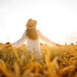 a woman standing amongst plants in a field during a sunset