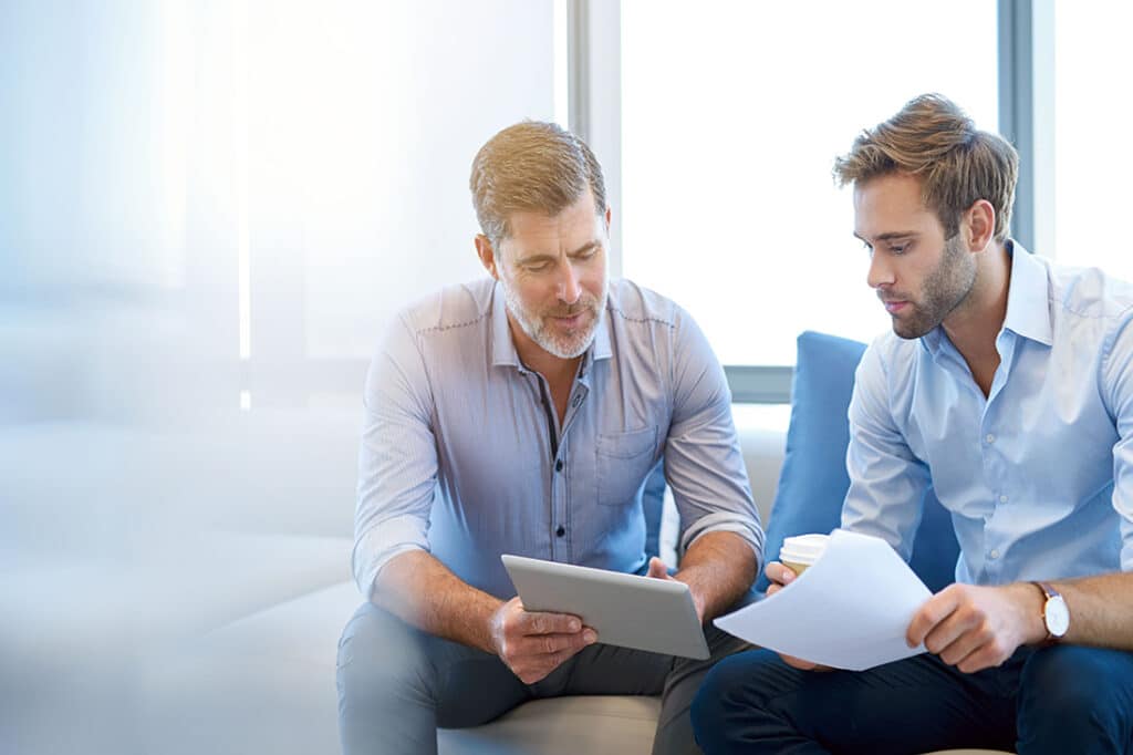 A sponsor using a digital tablet to discuss information with a younger colleague in a modern business lounge