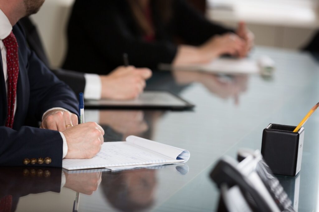 Close up shot of the hands of different people in suits sitting around a conference table.