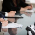 Close up shot of the hands of different people in suits sitting around a conference table.