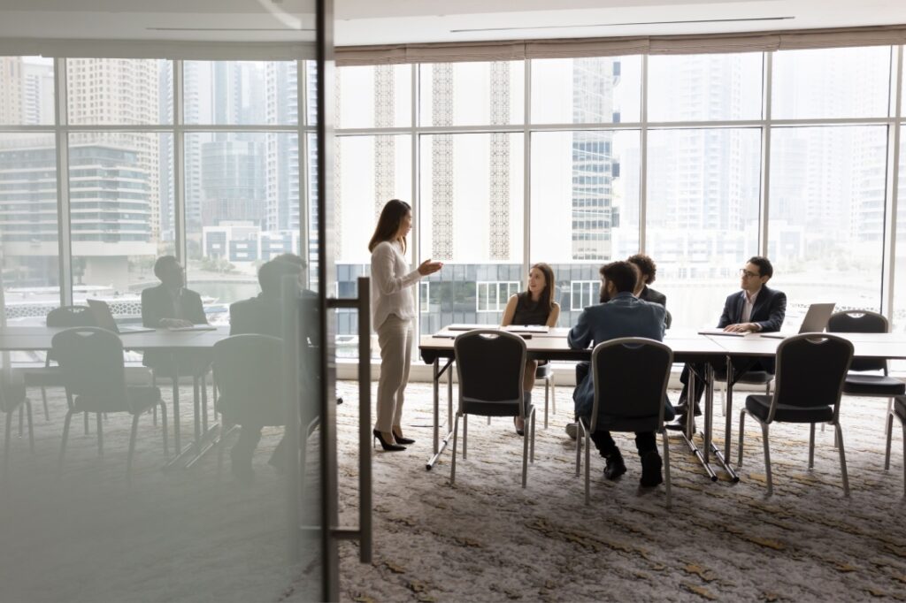 A wide shot of a woman giving a presentation in a conference room.