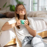 A smiling woman holds a cup of tea and enjoys being present in time