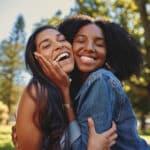 Close up lifestyle portrait of diverse multiracial happy best friends hugging each other and laughing in the park