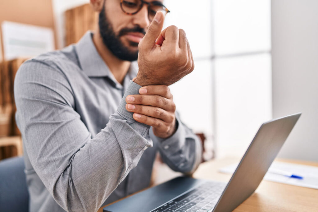 A man rubs his wrist while sitting at his desk.