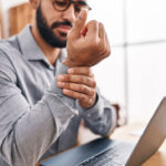 A man rubs his wrist while sitting at his desk.