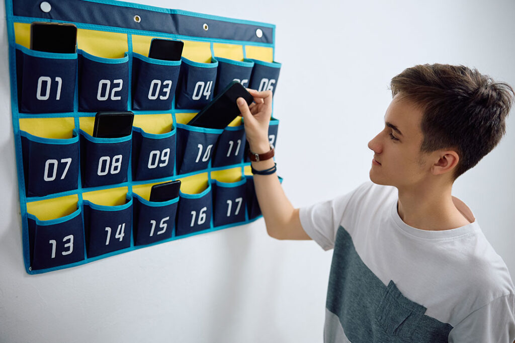High school student leaving his smart phone in cell phone organizer on the wall before entering the classroom at school