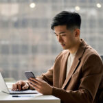 Man using cell phone looking working in corporate office with laptop computer