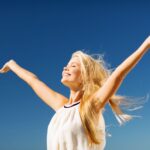 a woman smiling while raising her hands up towards the sky