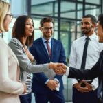 Five professionals shaking hands during a leadership transition to maintain company morale