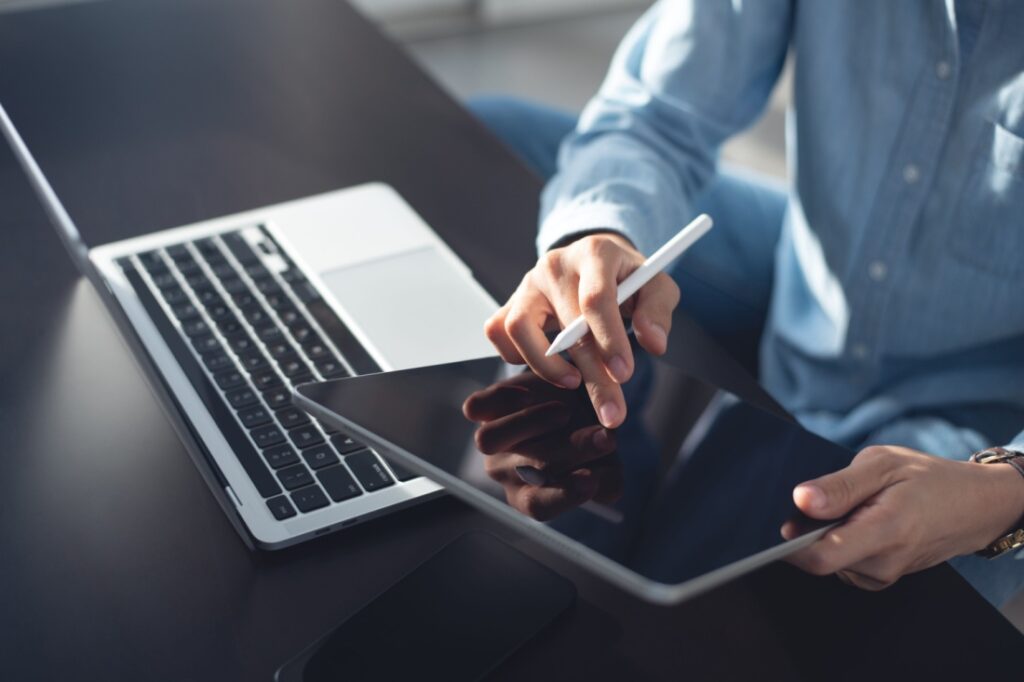 Hands holding up an iPad next to a laptop.