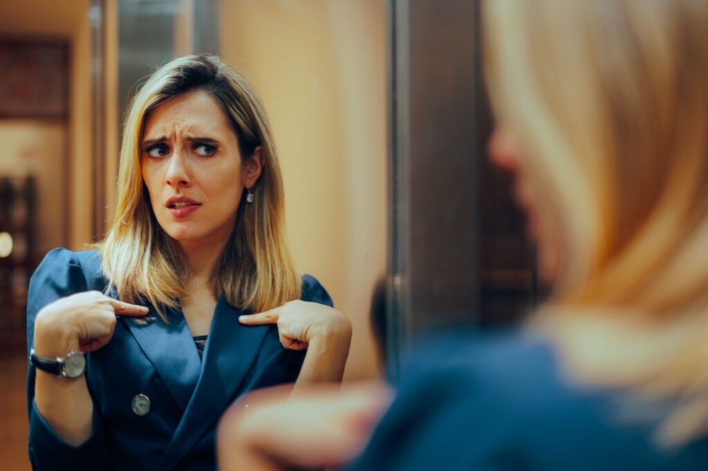 A woman looking at herself in the mirror skeptically.