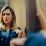 A woman looking at herself in the mirror skeptically.