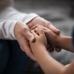 Close on an adult's hands embracing a child's hands.