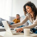 A woman writing on her laptop from a couch.