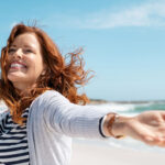 Happy mature woman with arms outstretched feeling the breeze at beach