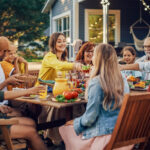 Group of friends or family gathering for a meal outdoors surrounding a table