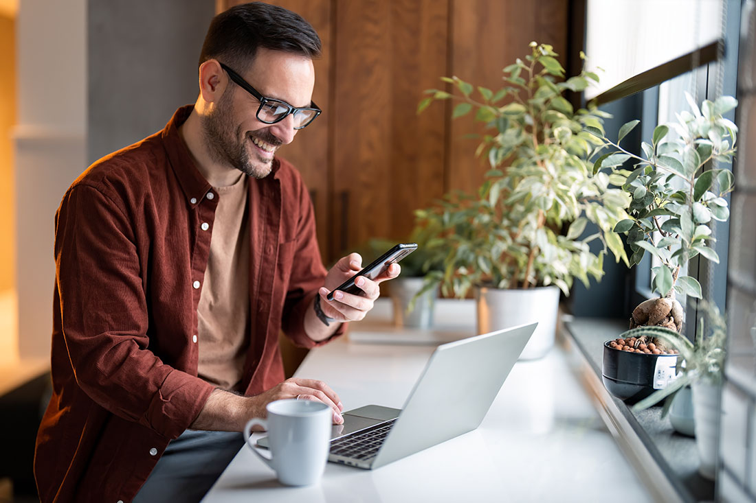 man in stylish casual clothes using smartphone and laptop computer