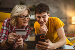 blonde woman and her teenager son shopping online use mobile phone and credit card