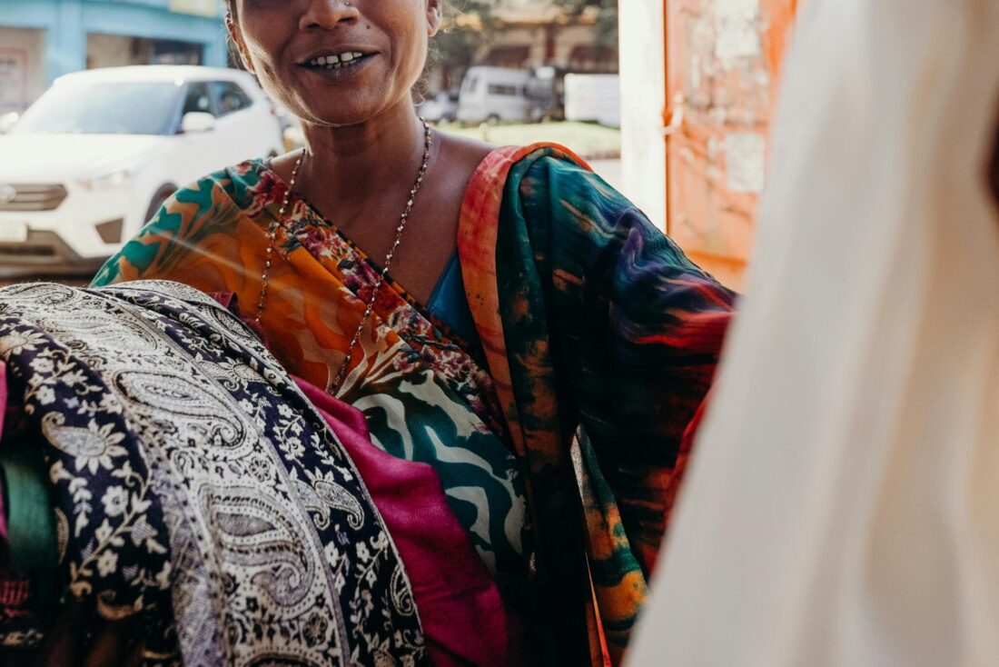 A woman dressed in a sari looks at hanging fabric.