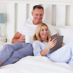 Couple Lying In Bed Looking At Digital Tablet Together