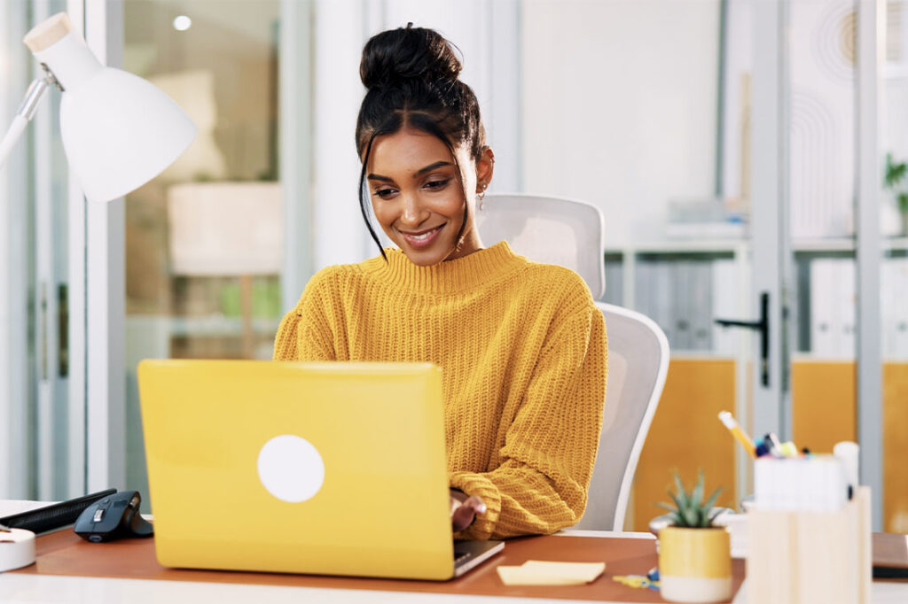 woman in yellow sweater on yellow laptop working