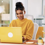 woman in yellow sweater on yellow laptop working