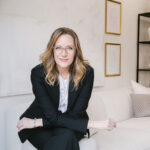 Allison Graham in suit on couch with arms crossed