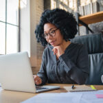Happy young African American woman businesswoman manager in casual formal wear eyeglasses looking at computer screen