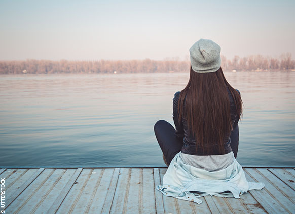 A woman sitting on a dock watching the water in peace and calm